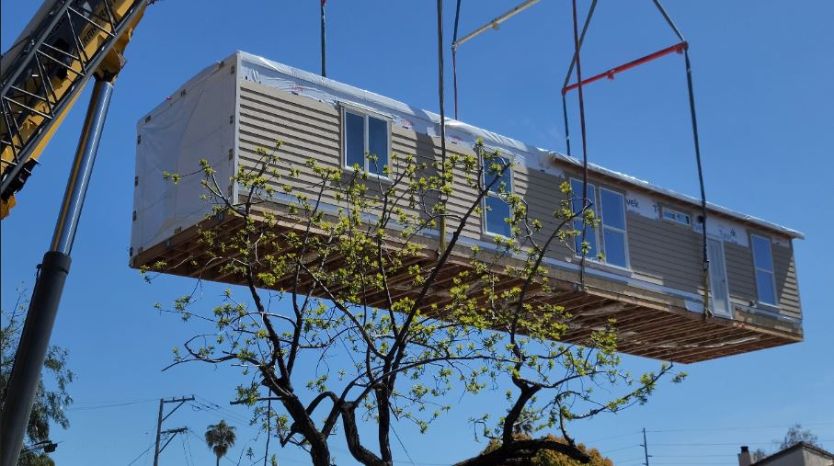 Logo depicting a modular home being lifted into place by a crane
