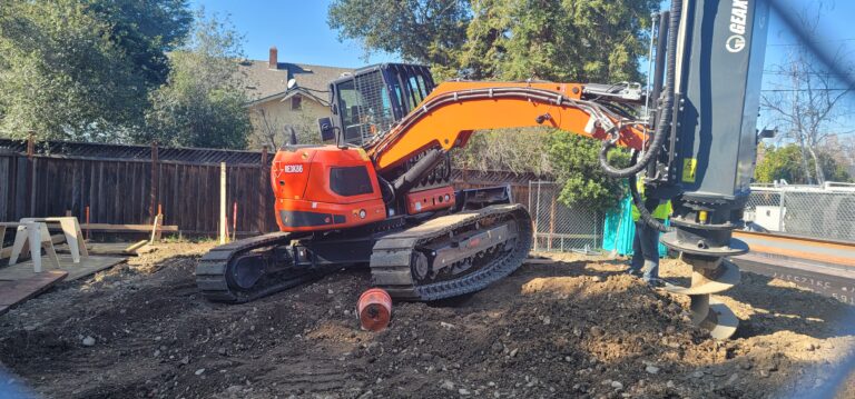 Excavator drilling for shoring on our urban infill lot as part of early site preparation for a modular home.